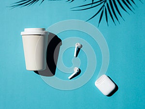 Cup of coffee to go and wireless headphones on blue background