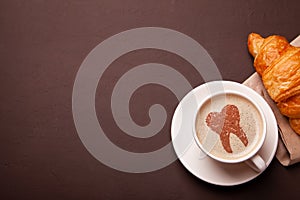 Cup of coffee with a tooth on foam. Coffee spoils teeth and makes them yellow. Morning coffee or coffee break with a croissant