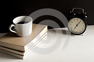 A cup of coffee on top the books with retro alarm clock.