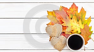 Cup of coffee with two burlap hearts and autumn leaves on white wooden table.Top view. Space for text