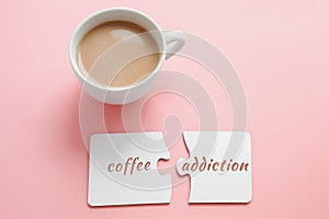 cup of coffee and two white disconnected puzzles with the inscription coffee addiction on a pink