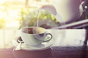 Cup of coffee with water splashing from hot pot on wooden