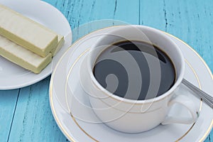 Cup of coffee and white chocolate wafer on blue ackground