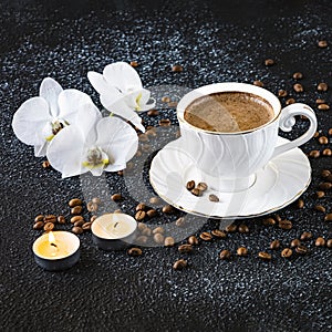 A cup of coffee, white orchid flowers, coffee beans and white candles. Romantic composition