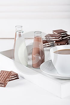 Cup of coffee on a white tray with brown cookies and chocolate m