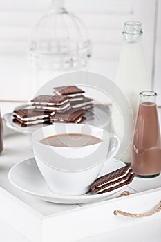 Cup of coffee on a white tray with cookies and chocolate milkshakes and milk