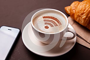 Cup of coffee with WiFi sign on foam. Free access point to the Internet WiFi. I like coffee break with croissant