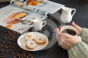 Cup of coffee in woman hands. Saucer with cookies, roasted coffee beans