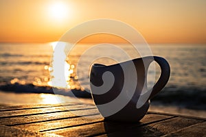 Cup of coffee on wood table at sunset or sunrise beach