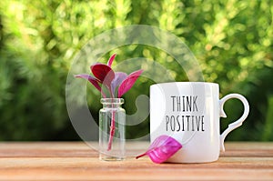 A cup of coffee on a wooden table in the garden with the text think positive