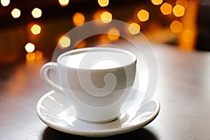 A cup of coffee on wooden table. Lights on the background. Front view
