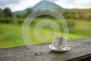 Cup of coffee on a wooden table over mountains landscape and rice field with sunlight. Beauty nature background