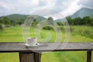 Cup of coffee on a wooden table over mountains landscape and rice field with sunlight. Beauty nature background