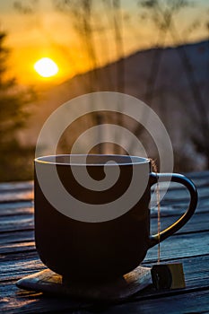 The cup with coffee on the wooden table during the sunset