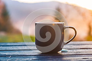 The cup with coffee on the wooden table during the sunset