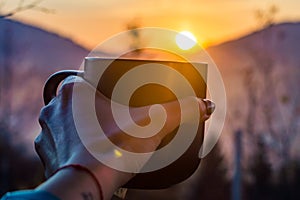 The cup with coffee on the wooden table during the sunset