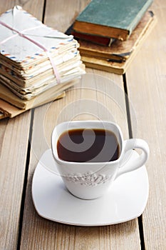 Cup of coffee on wooden table. Vintage books and pile of letters