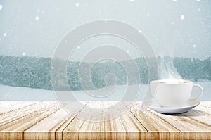 Cup of coffee on wooden table with winter snowfall covered fores