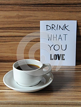 A cup of coffee on wooden zebrano background. Inscription drink what you love