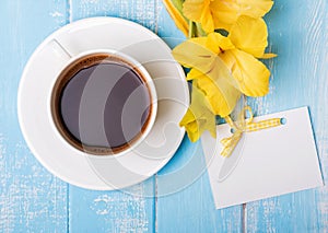 Cup of coffee, yellow flowers and blank paper card on blue woode