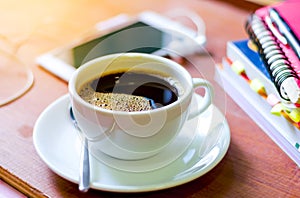 Cup of dark coffee with smart phone and book on wooden background. Coffee can help in your education time