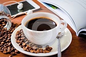 Cup of dark coffee ,smart phone with coffee beans and a magazine on wooden background. Relax time concept