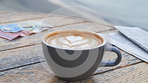 Cup of delicious coffee, newspaper and banknotes on wooden table, closeup