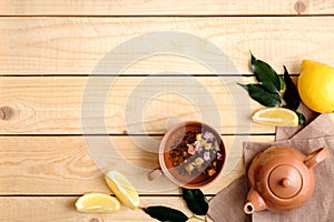 Cup of dried herbal tea, teapot, lemon, plants leaves and ginger root on rustic wooden background, view from above, flat lay