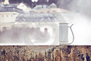 Cup for drinking mineral water standing on basin of hot spring Vridlo and vapor rising on background