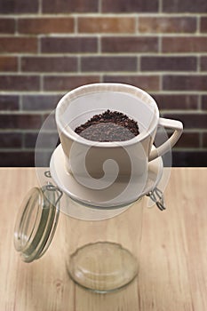 Cup of drip coffee with paper filter tool on wood table and brick wall