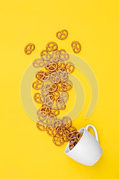 A cup with effuse pretzels on yellow background, flat lay.