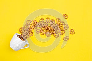 A cup with effuse pretzels on yellow background, flat lay.