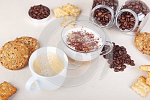 Cup of espresso, cappuccino with chocolate crumbs, cookies, crackers and coffee beans on table