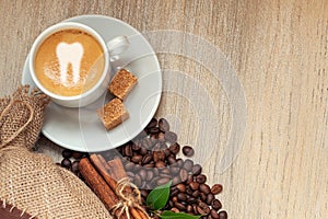 Cup with espresso with coffee beans, burlap sack and cinnamon on light wooden background