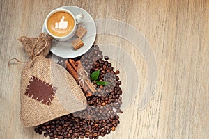 Cup with espresso with coffee beans, burlap sack and cinnamon on light wooden background. With like sign on coffee foam