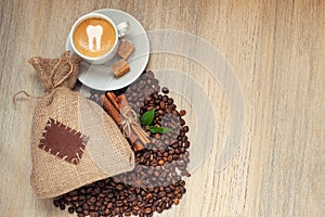 Cup with espresso with coffee beans, burlap sack and cinnamon on light wooden background