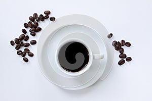 Cup of espresso coffee with saucer and coffee beans scattered around on white background. Top view. Close up image