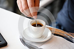 Cup espresso coffee on table with plate and spoon. Coffee time concept. Stir sugar in coffee cup. Male hand hold spoon
