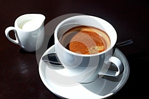 A cup of espresso and a creamer with milk