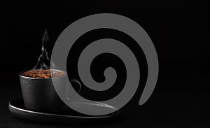 Cup with espresso with foam on a saucer. Steam rises over a cup of coffee. Black stone background. Copy space for text. Close-up,