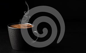 A cup of espresso with foam, steam rises above a cup of coffee. Black stone background. Copy space for text. Close-up, shallow