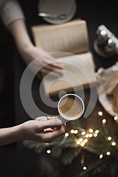 Cup of espresso in girl`s hand and book, dark photo, selective focus, cozy christmas winter photo, top view