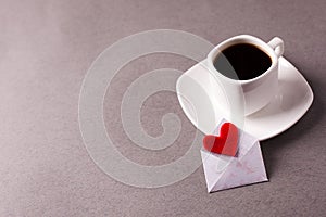 A cup of espresso and a love message in a small envelope on a gray background, laconism, minimalism.
