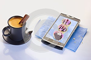 A cup of espresso with a tube of cinnamon. Dessert on a paper napkin in a smartphone. Chocolate paste in a basket of shortcrust pa