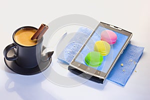 A cup of espresso with a tube of cinnamon. Dessert on a paper napkin in a smartphone. Pasta brownies, red, green yellow.