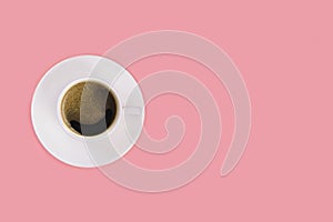 Cup of espresso on a white saucer on a pink background.