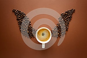 Cup of espresso with wings from coffee beans on brown background. Good morning concept. Top view. Flat lay.