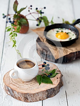 A cup of espresso on a wooden stand in the foreground. Fried chicken egg in the pan for breakfast. Healthy organic foods. Close-up