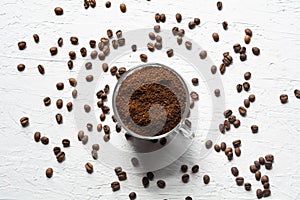 A Cup filled with coffee beans. Coffee beans are scattered on the white surface of the table