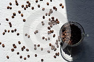 A Cup filled with coffee beans. Coffee beans are scattered on the white surface of the table